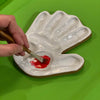 hand made, ceramic palette, modeled after the hand of the artist that made the watercolor mixing palette being used with a watercolor brush and paint