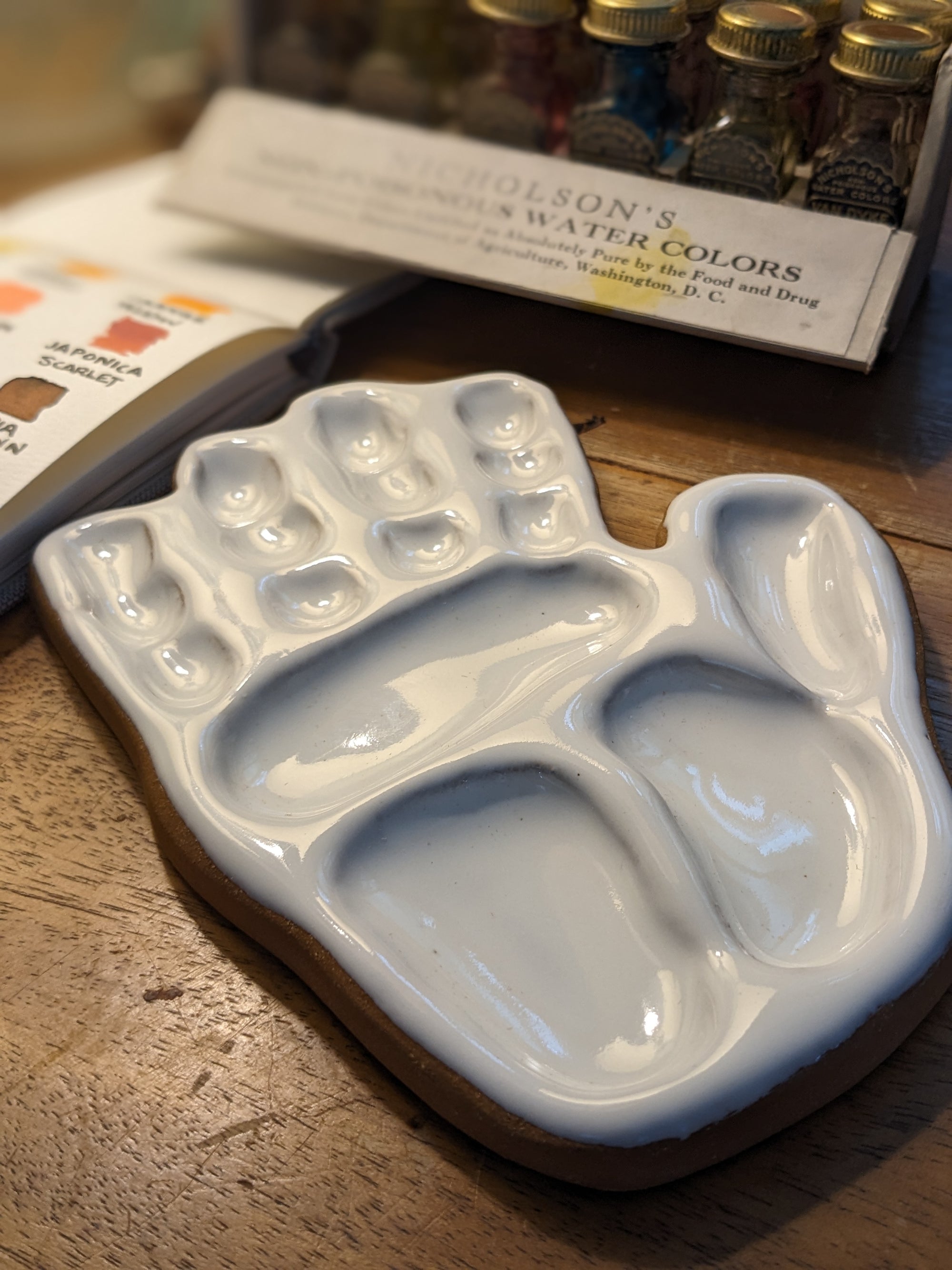 hand made, ceramic palette, modeled after the hand of the artist that made the watercolor mixing palette with peerless liquid watercolors in the background