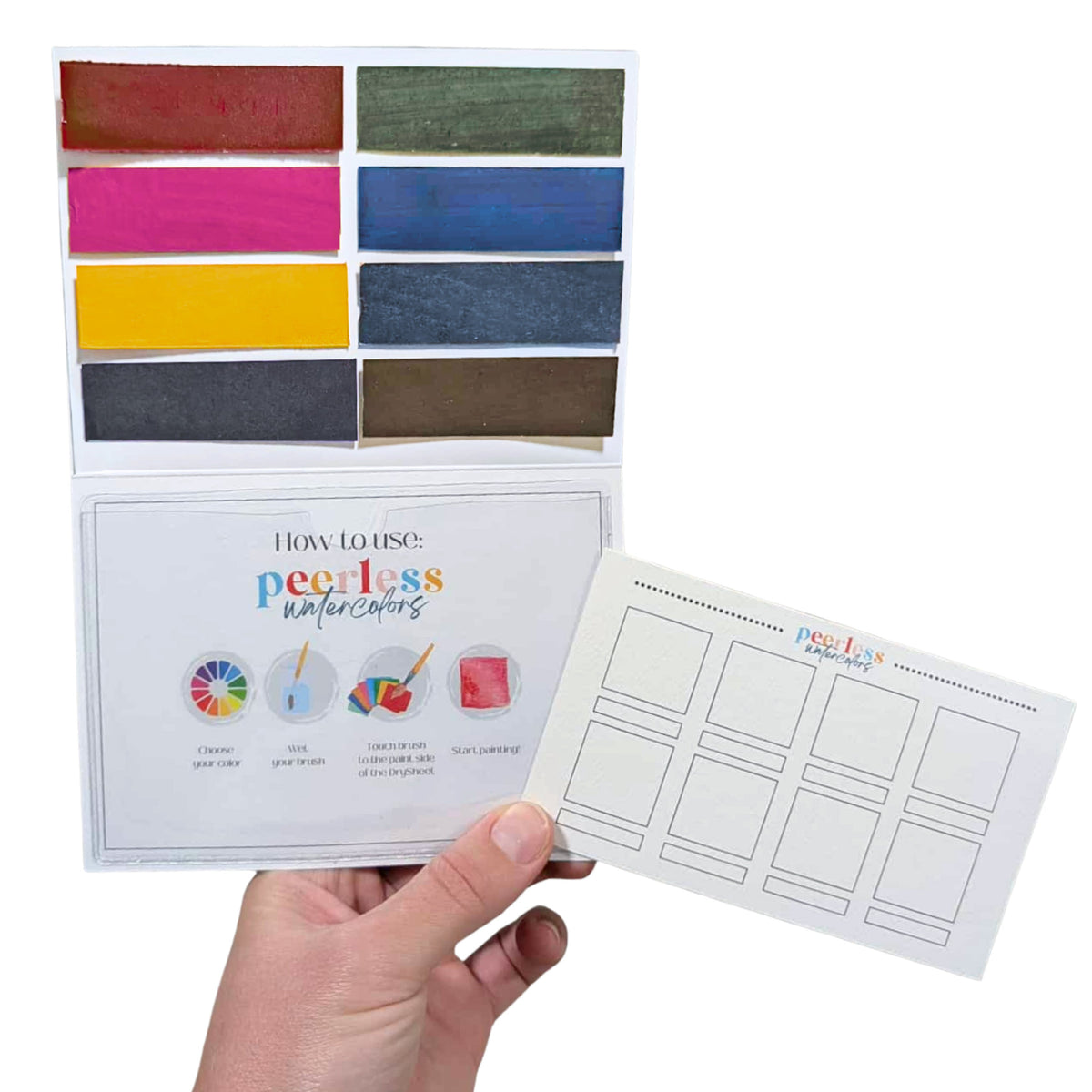 A hand holds a Urban Sketcher Starter Palette - a  Peerless Watercolors custom palette including 8 handpicked colors, an instructions card and a swatch card.